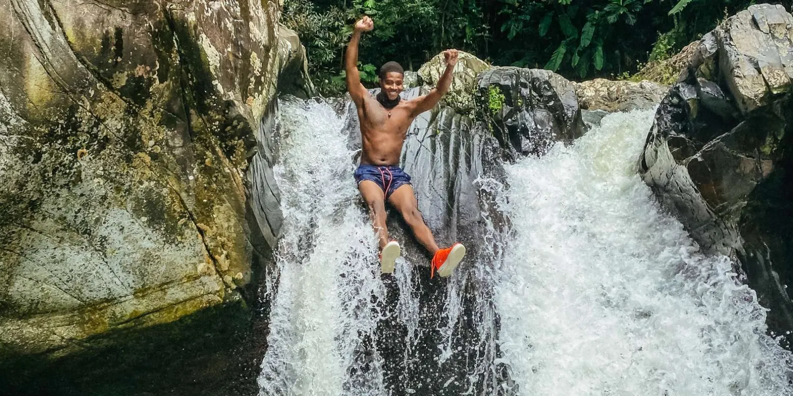 A guest riding the natural rock waterslide with both arms raised, El Yunque