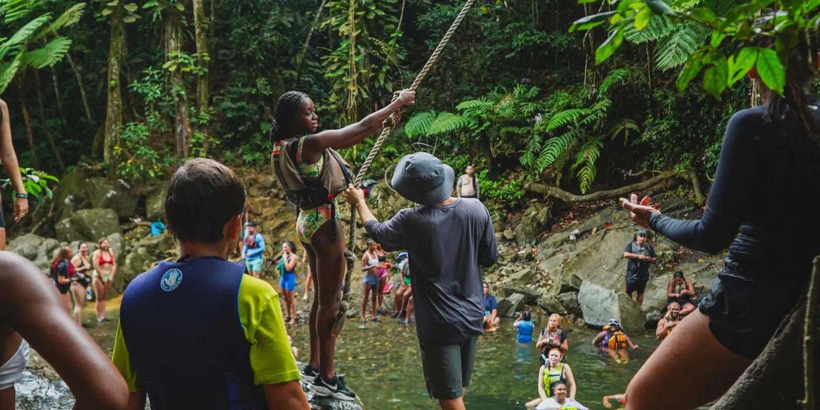 A group waiting their turn at the rope swing above the river pool