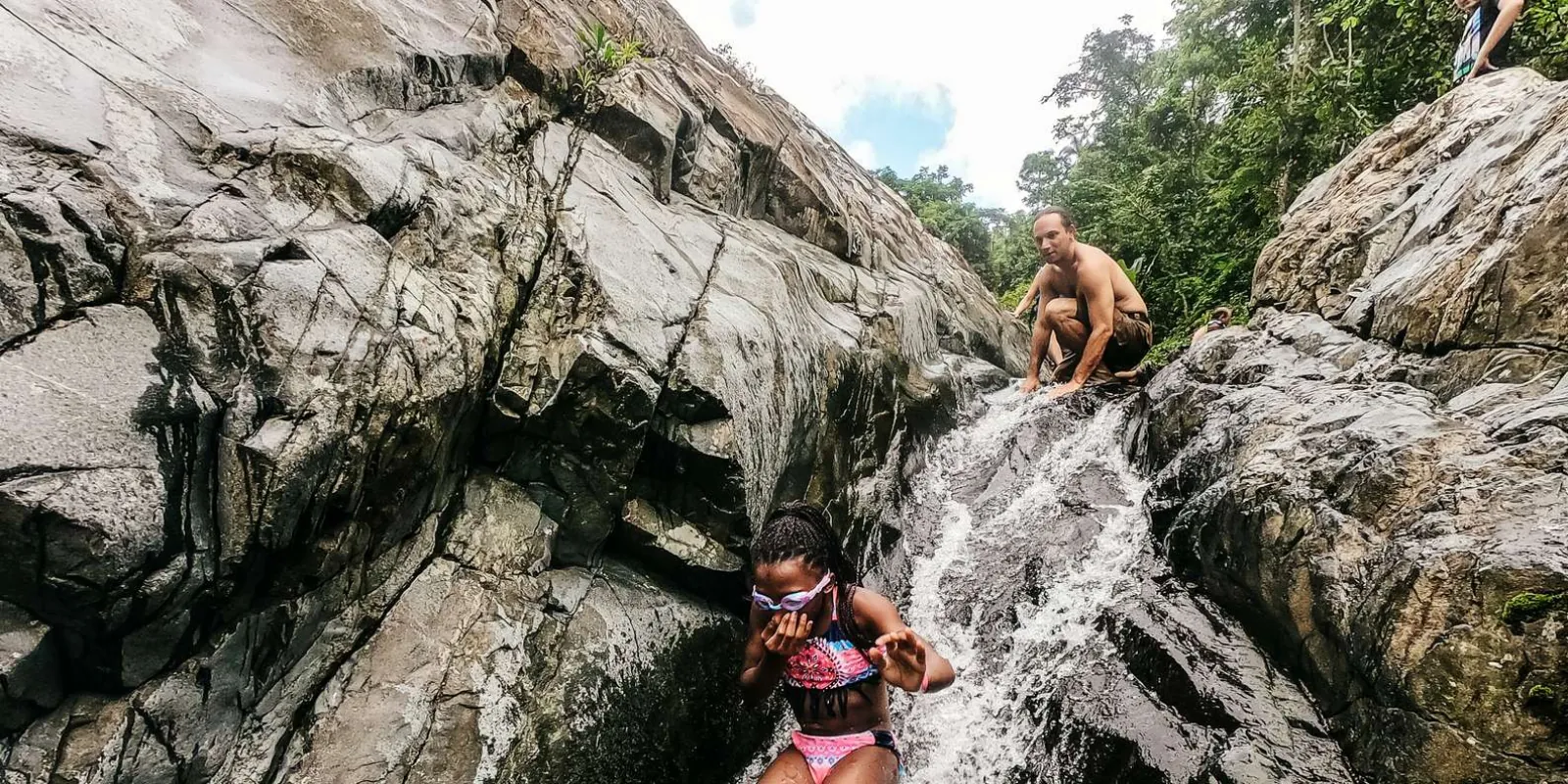 Guests picking their way down wet boulders beside the falls