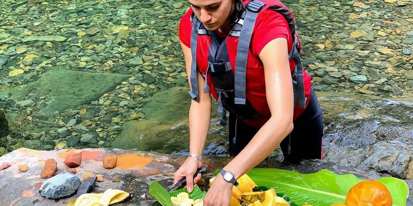 A guide cutting fresh local fruit on a leaf beside the river