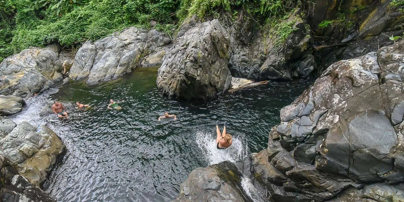 Swimmers spread across a wide river pool between the boulders
