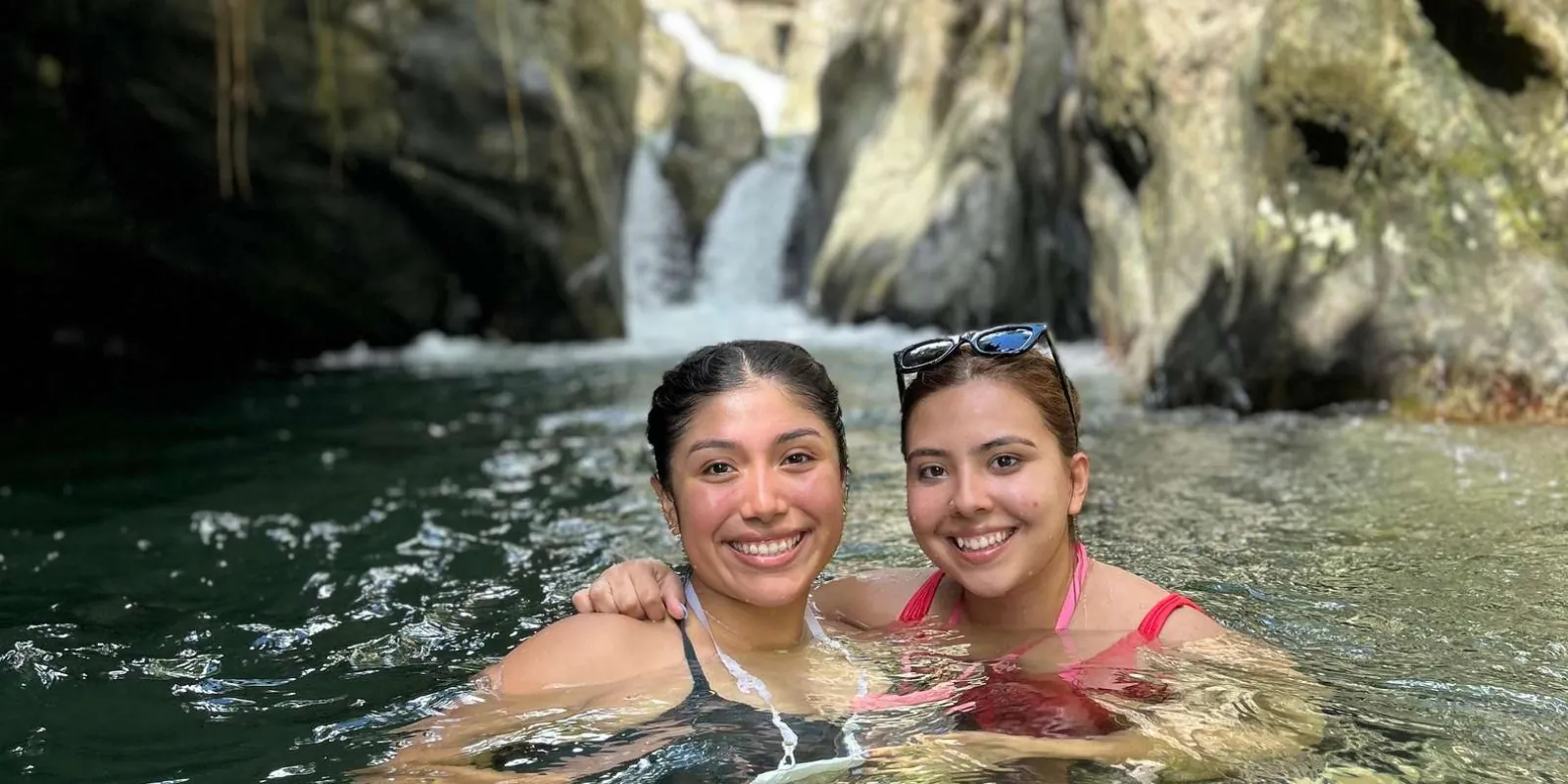 Two guests swimming in the clear river pool below the falls